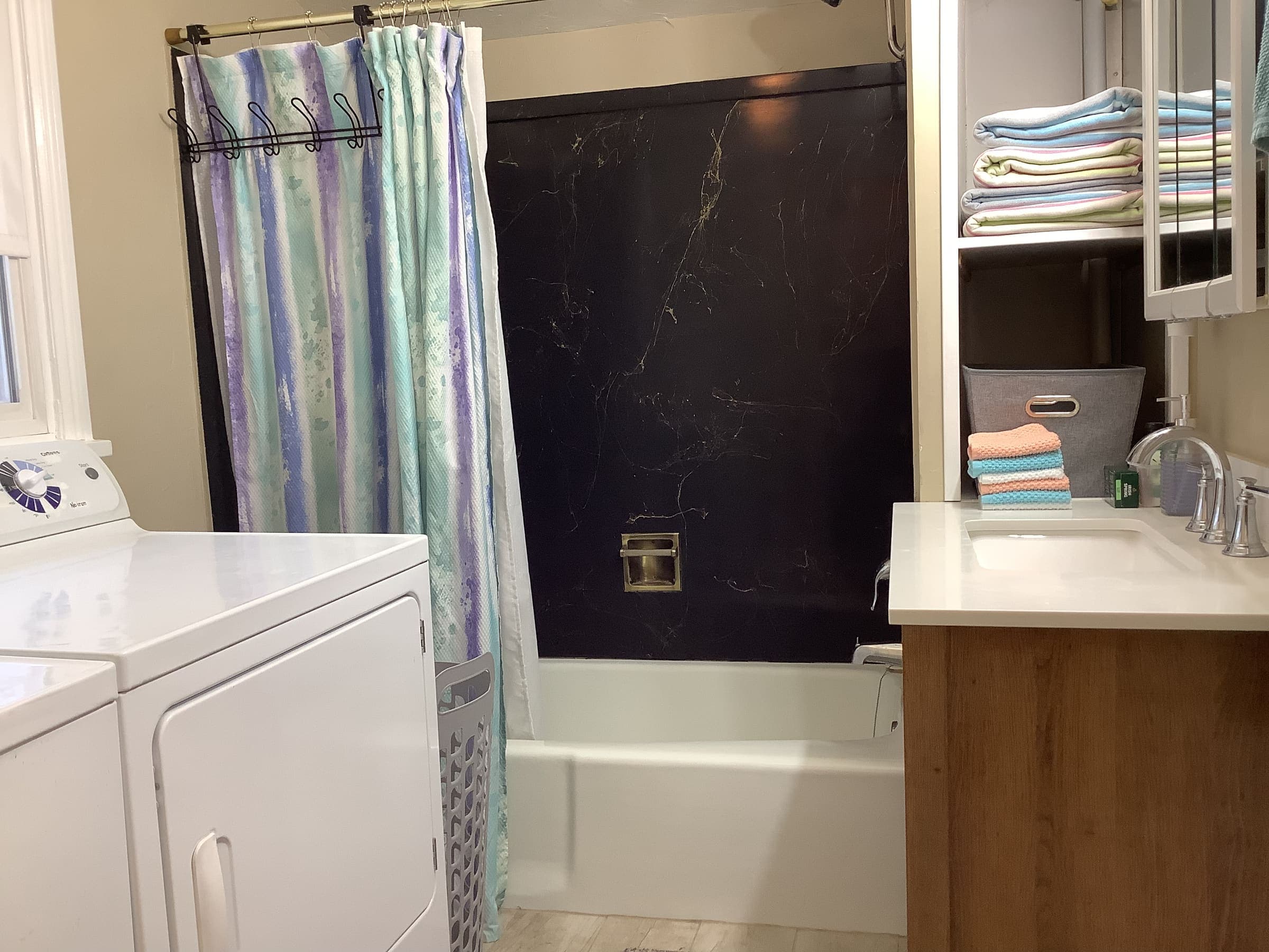Bathroom with a tub-and-shower combo and vanity, with a washer and dryer along the same wall