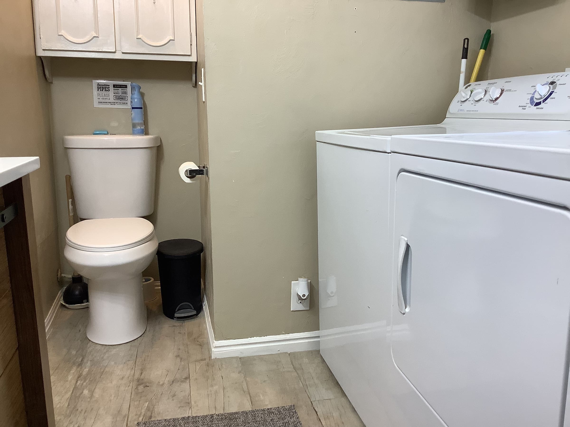 Bathroom with a toilet and a side-by-side washer and dryer, with wood-look flooring