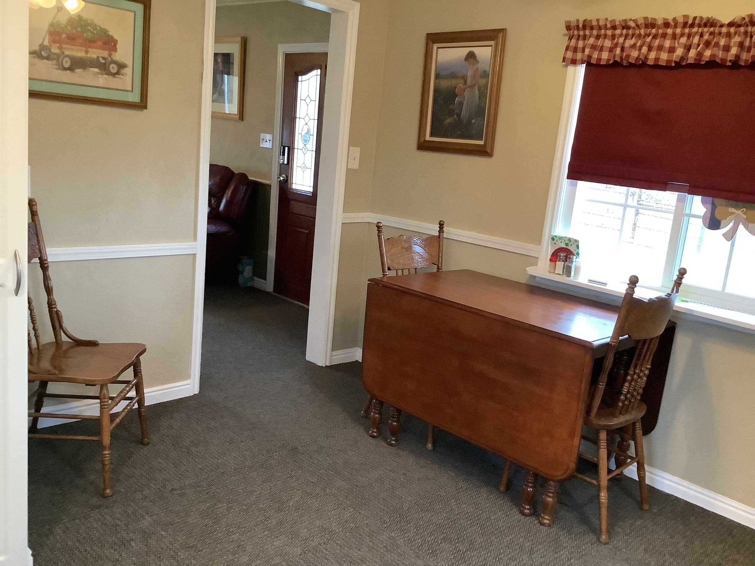 Drop-leaf dining table for two near the front entrance, with red curtains and farmhouse trim