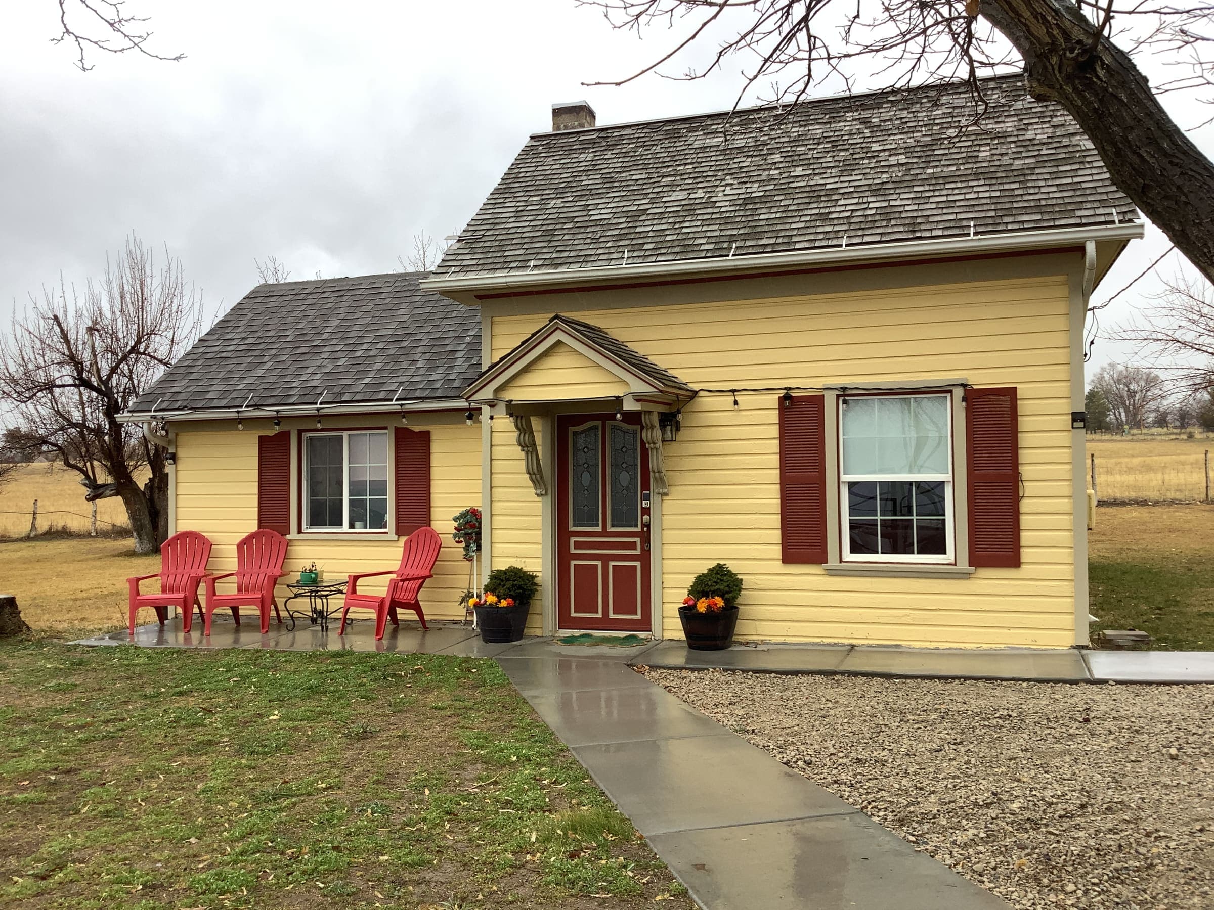 Front door and red shutters of the farmhouse, with red Adirondack chairs along the front walkway