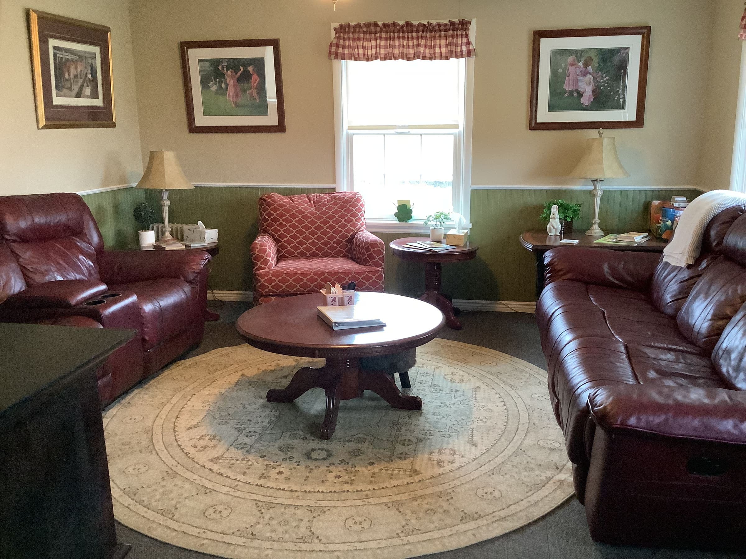 Front room seating area with two maroon leather couches, a round area rug, and coffee table