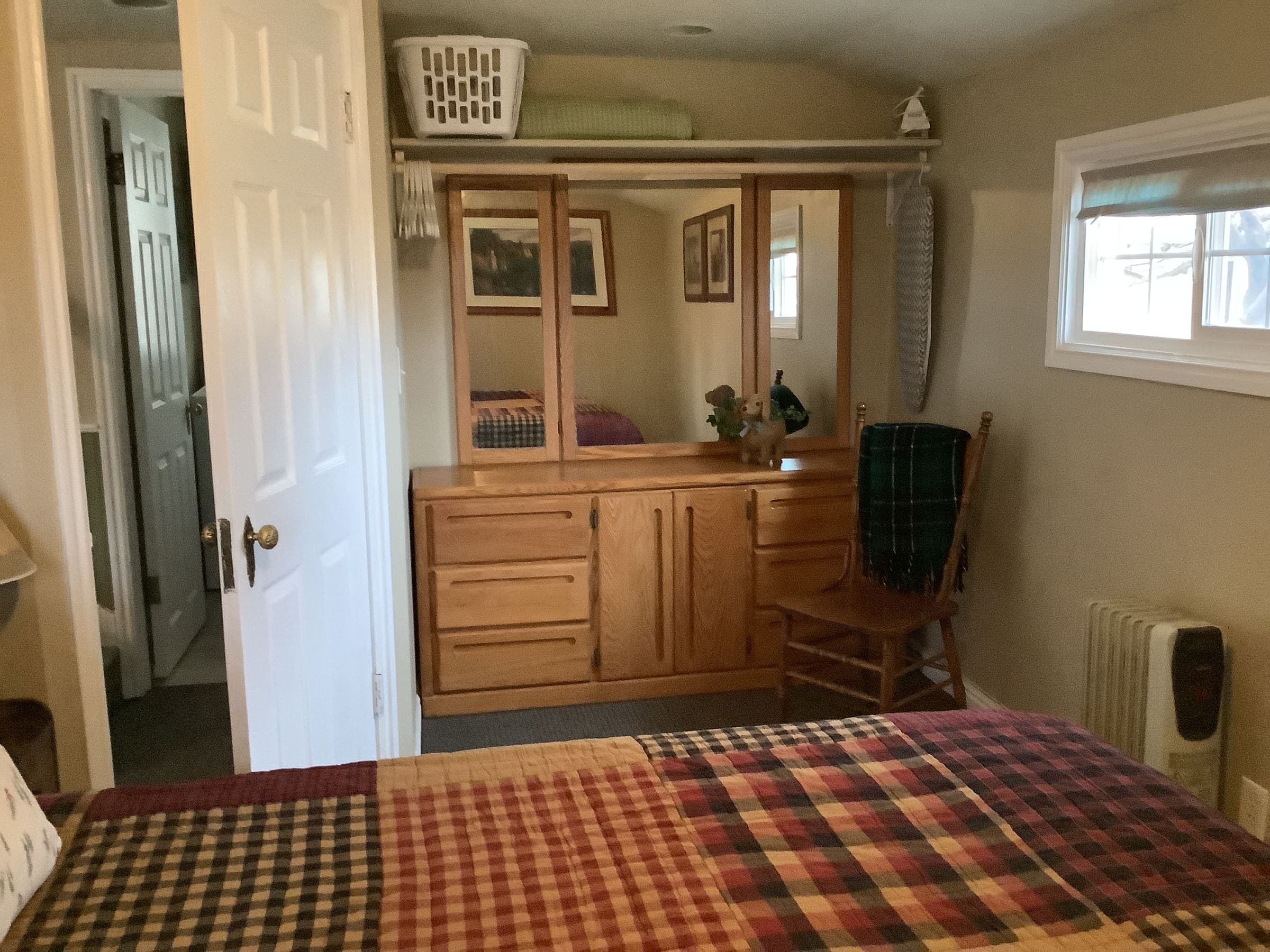 Master bedroom wardrobe area with a wood dresser, standing mirror, and the foot of the quilted bed