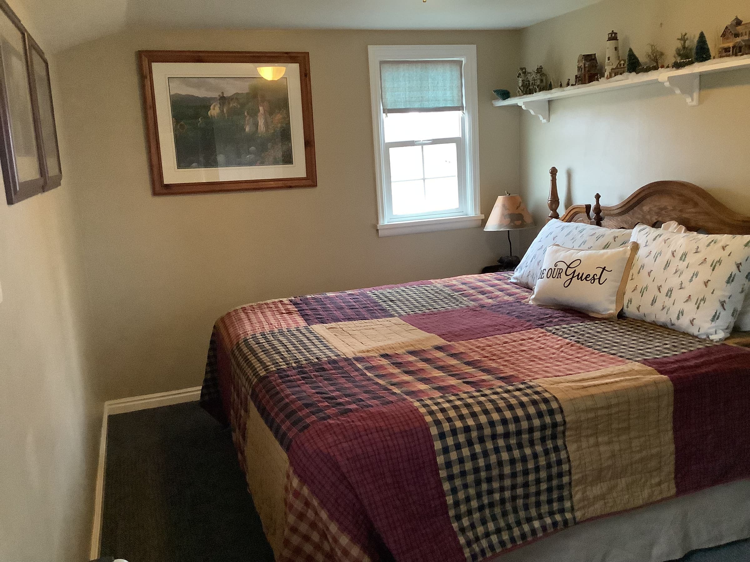 King-size master bedroom bed with a red plaid patchwork quilt, wood headboard, and a small shelf nightstand